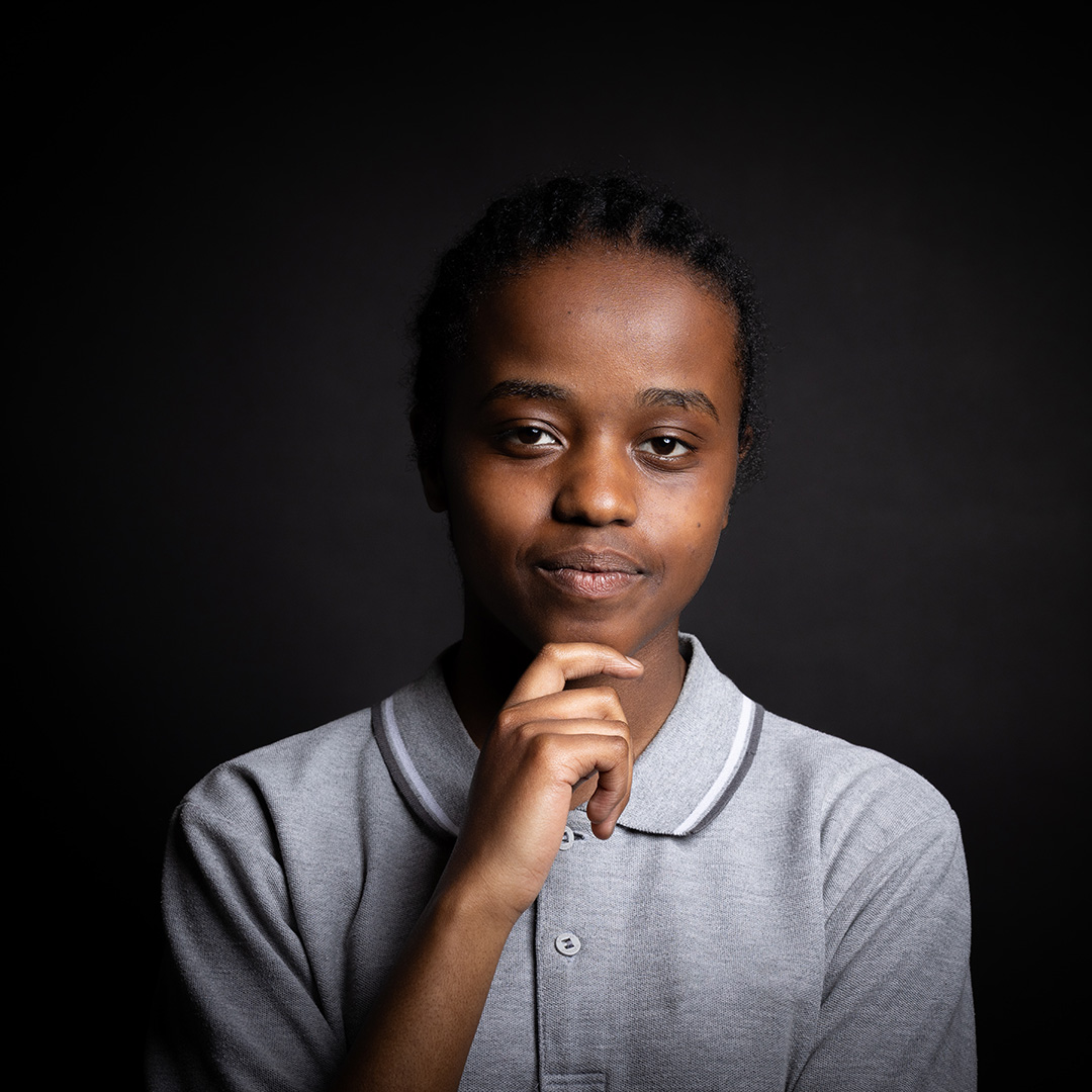 Sophia - Richmond upon Thames Travel & Tourism student - she is holding her hand up to her chin and wearing a grey polo shirt that is buttoned up.  