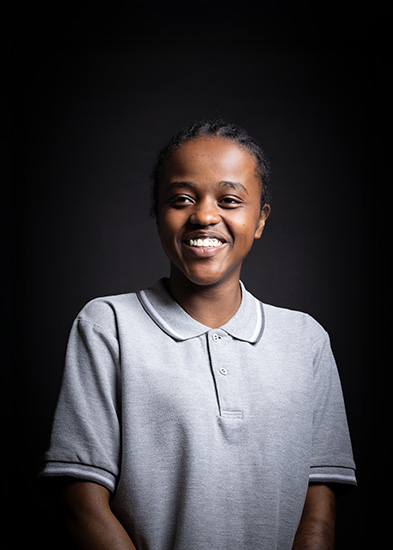 Sophia - Richmond upon Thames Travel & Tourism student - she is smiling and looking off into the distance, wearing a grey polo shirt that is buttoned up with a black background behind her.