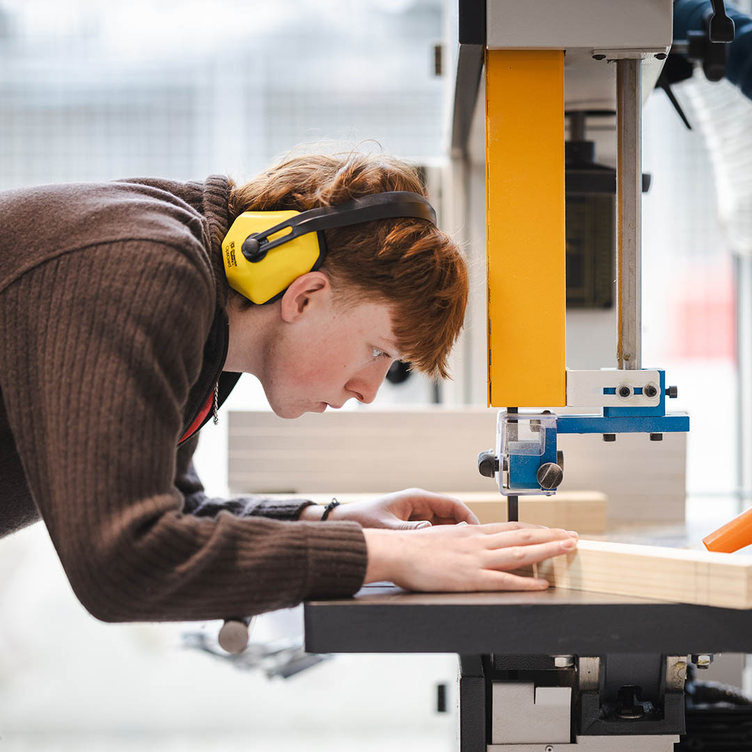 Richmond upon Thames student sawing some wood using a jigsaw machine and wearing yellow ear protectors