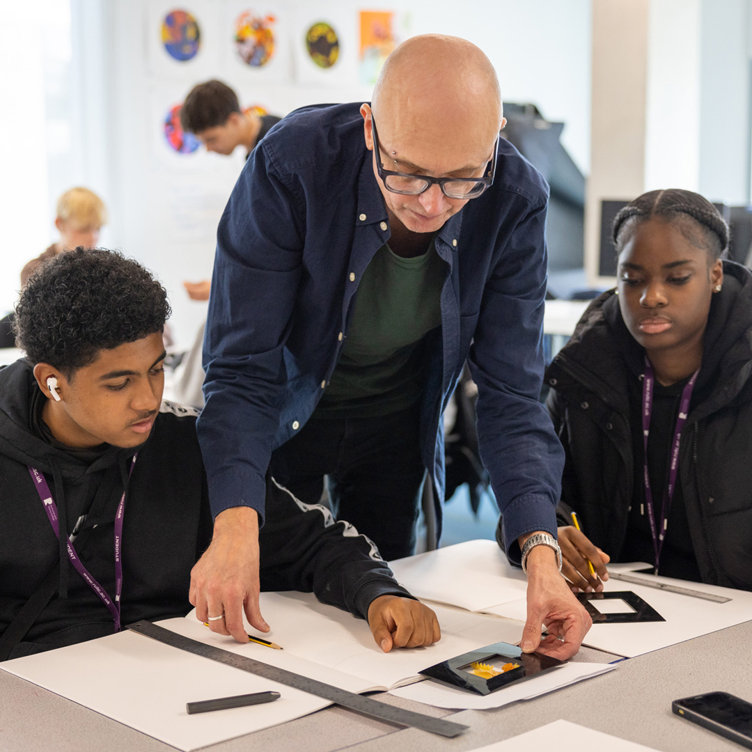 2 students at a table with a teacher helping them