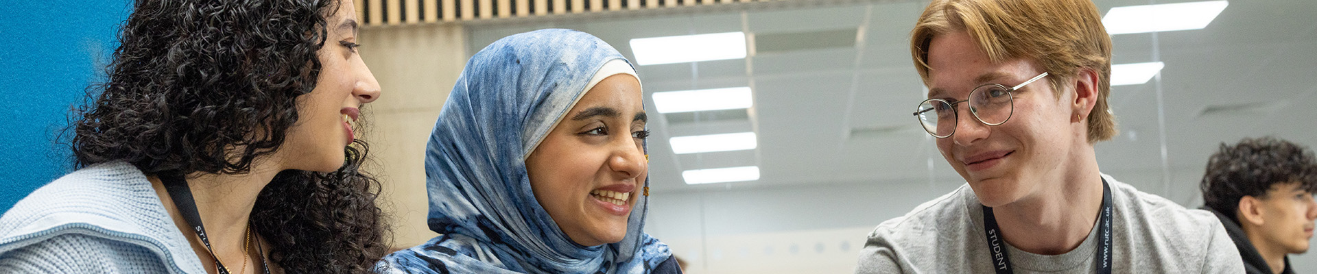Three Richmond upon Thames students sitting and talking together. Two female and one male student who is wearing glasses and smiling.