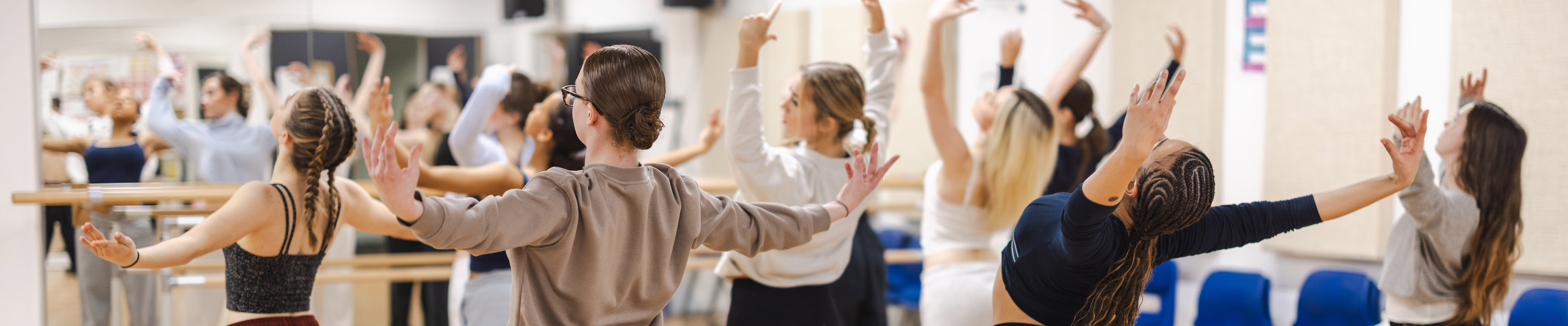 Richmond upon Thames dances in the dance studio. They are facing the mirrors and bar and their arms are out stretched.