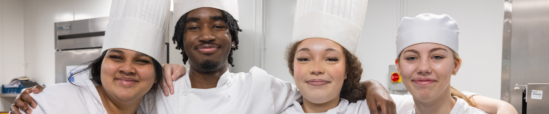 four professional cookery students in chef whites, smiling at the camera