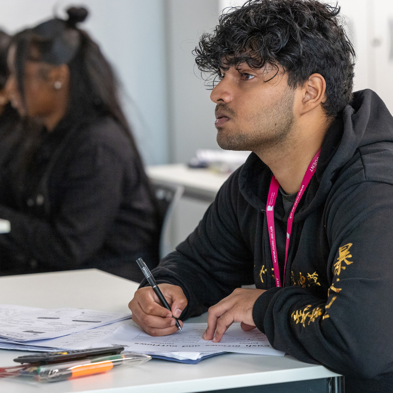 male student sitting at a desk in a classroom taking notes