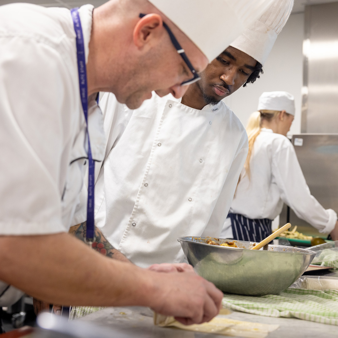 a student being supported by a teacher in a kitchen making food in chef whites