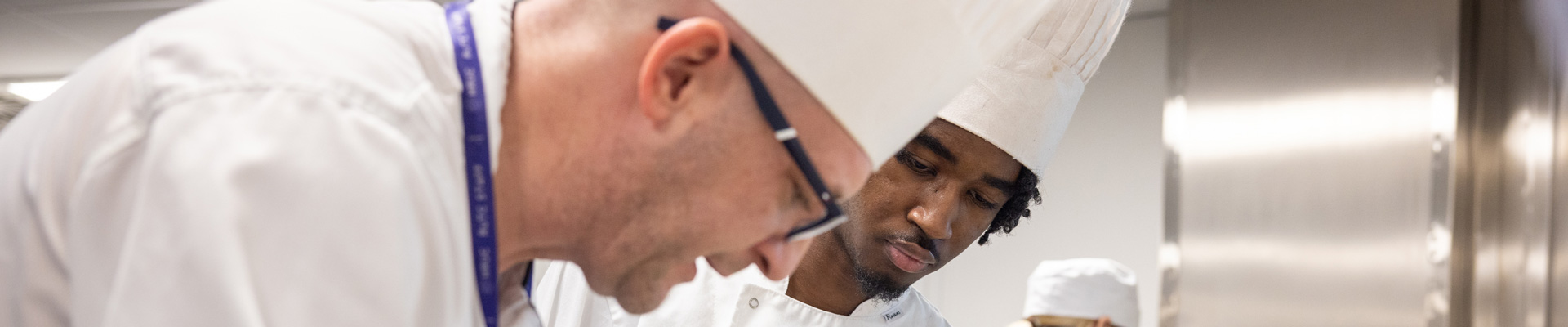 cookery teacher supporting student both in chef whites