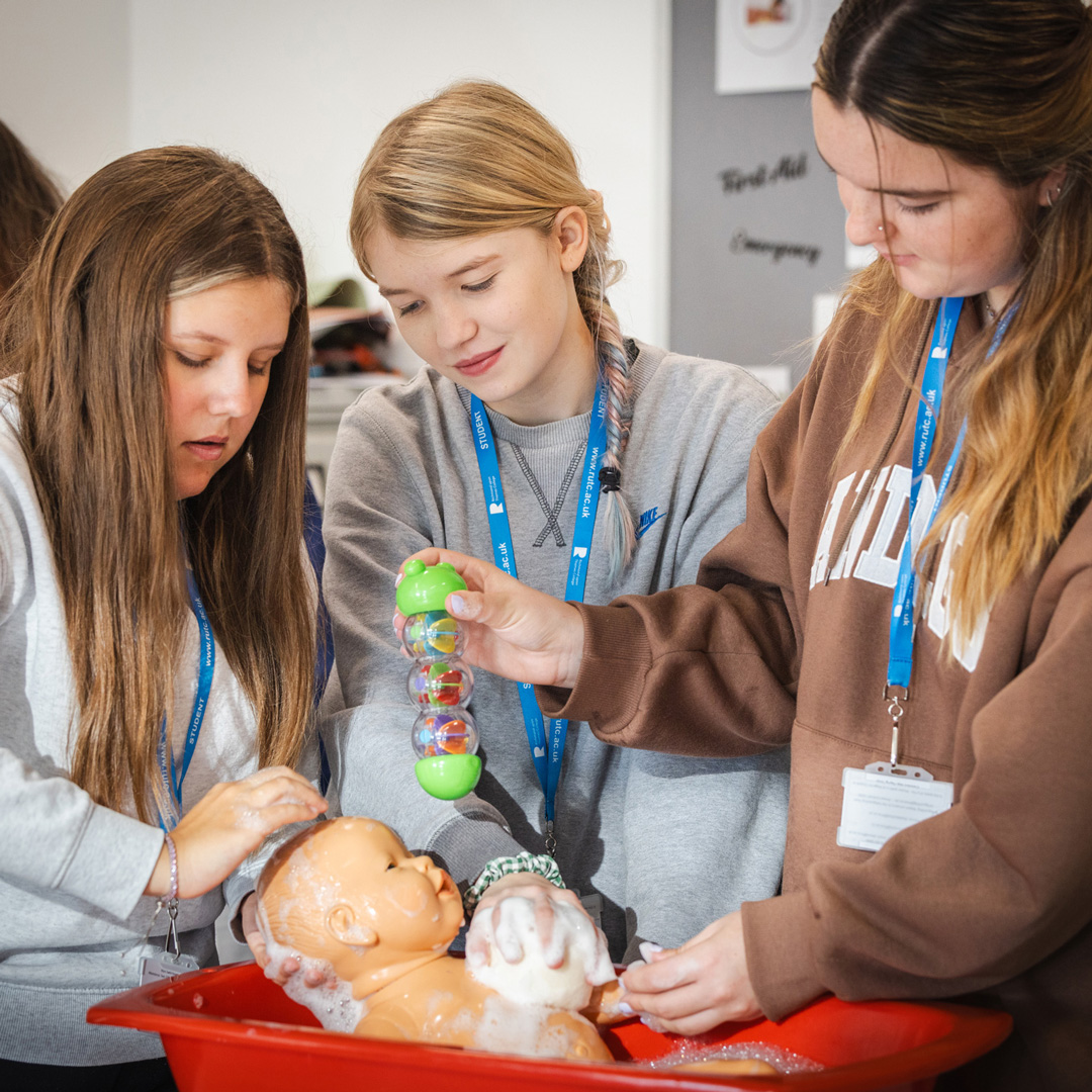 three female students washing a doll in a bath