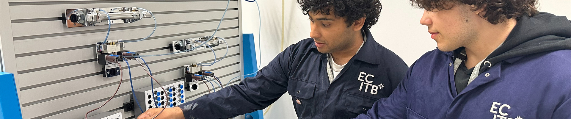 Two Richmond students working on electro-pneumatics together, wearing ECITB blue overalls.