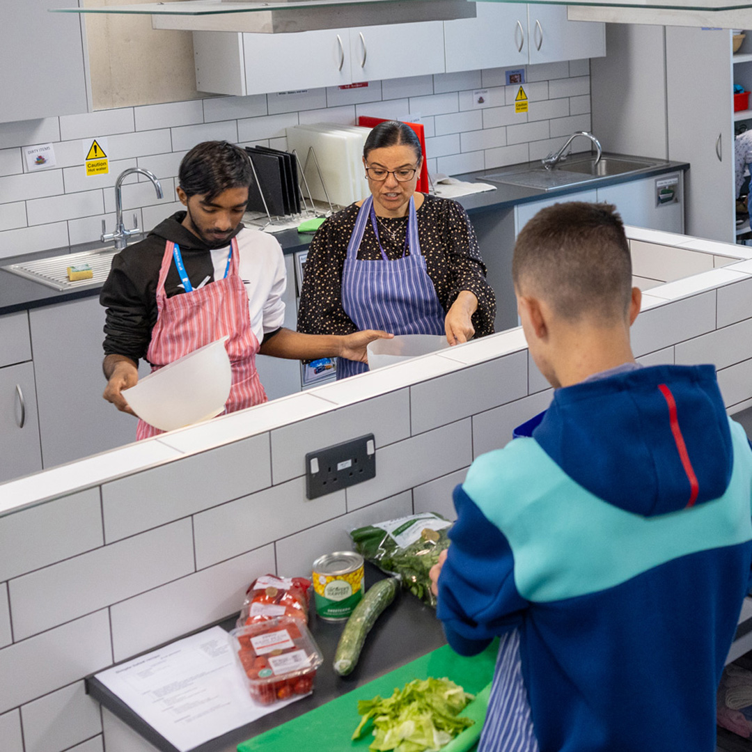 2 students and a teacher in a kitchen preparing food