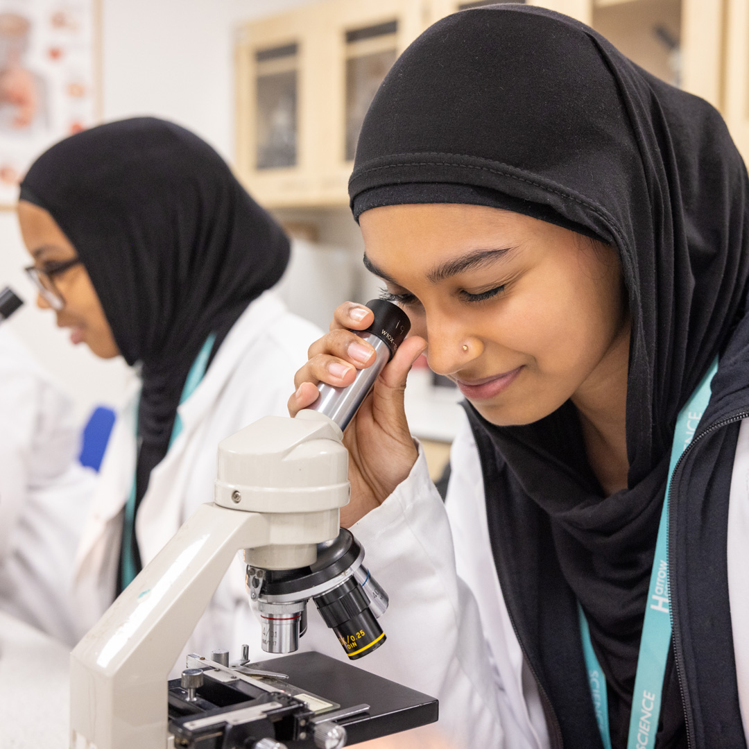 female student in a lab coat using a microscope