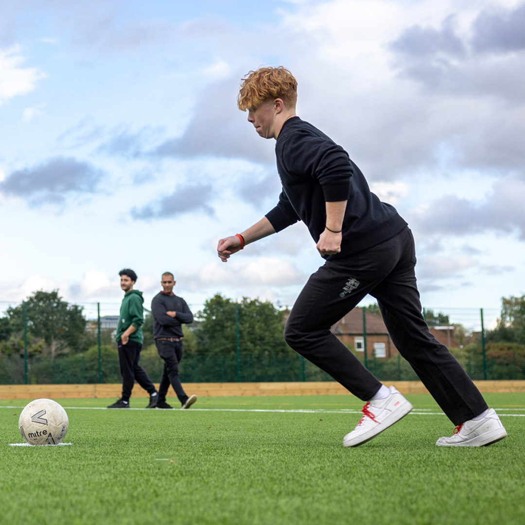 male student on football pitch kicking a ball
