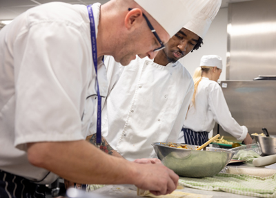 catering teacher showing student how to make something in the kitchen in their chef whites