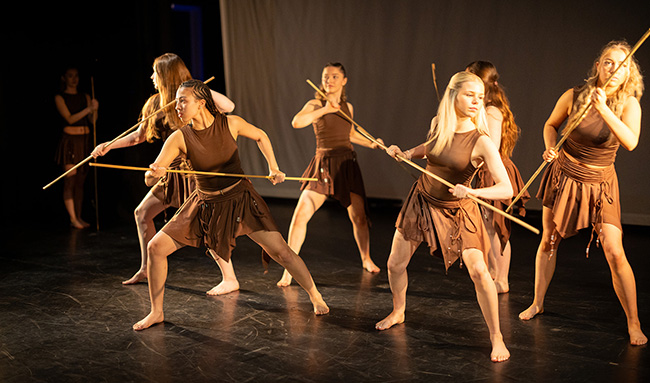 IGNITE Festival Richmond Performers - they are all wearing brown skirts and tank tops and holding yellow staffs