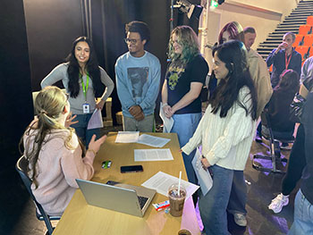Students standing around a table speaking to a lady at the philosophy conference