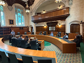 Politics students in UK Supreme Court room, which has green carpets and big circular wooden desks.