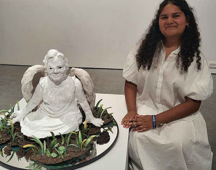 Female Art student sitting with ceramic sculpture of grandmother at UAL Origins Creatives Exhibition