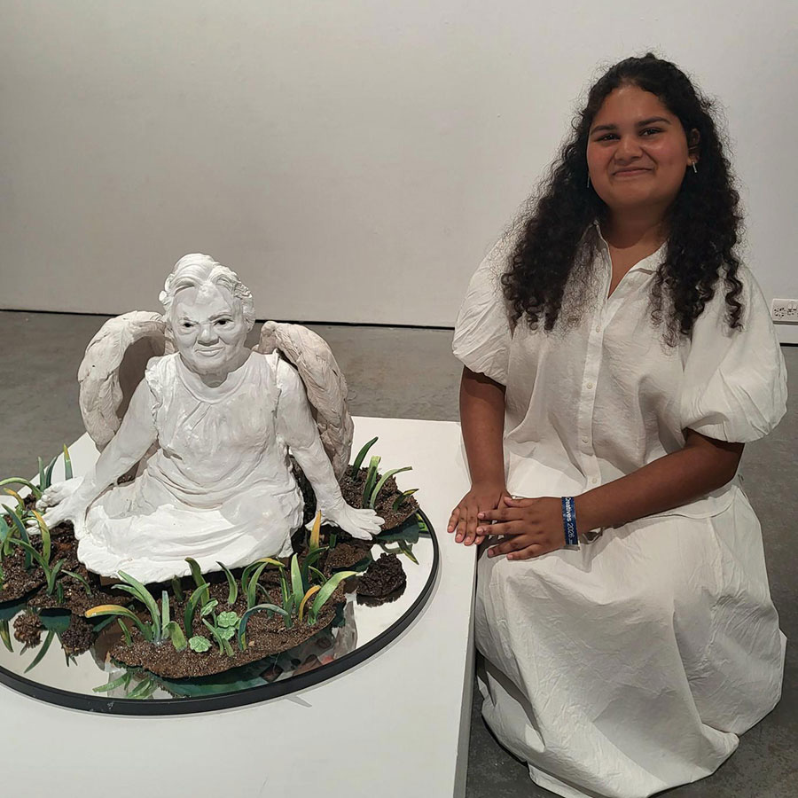 Female Art student sitting with ceramic sculpture of grandmother at UAL Origins Creatives Exhibition
