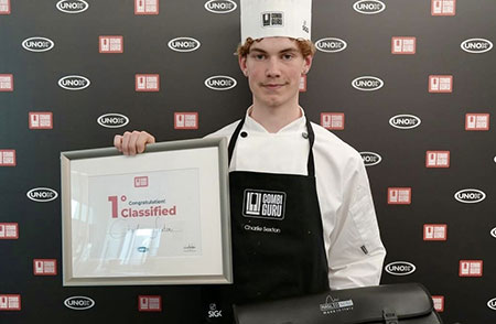Student, Charlie Sexton, pictured wearing chef whites and hat, holding a framed certificate for winning the Combiguru Challenge