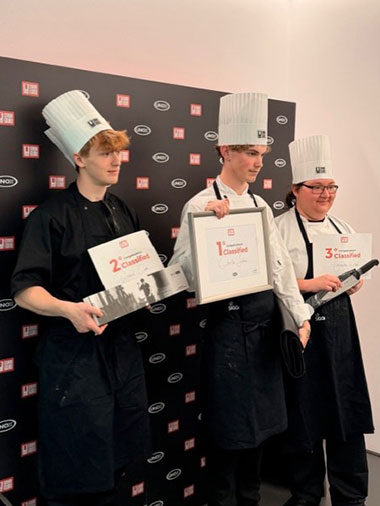 three HRUC catering students, including winner, Charlie Sexton, standing in a row in their chef whites, holding their certificates for the camera