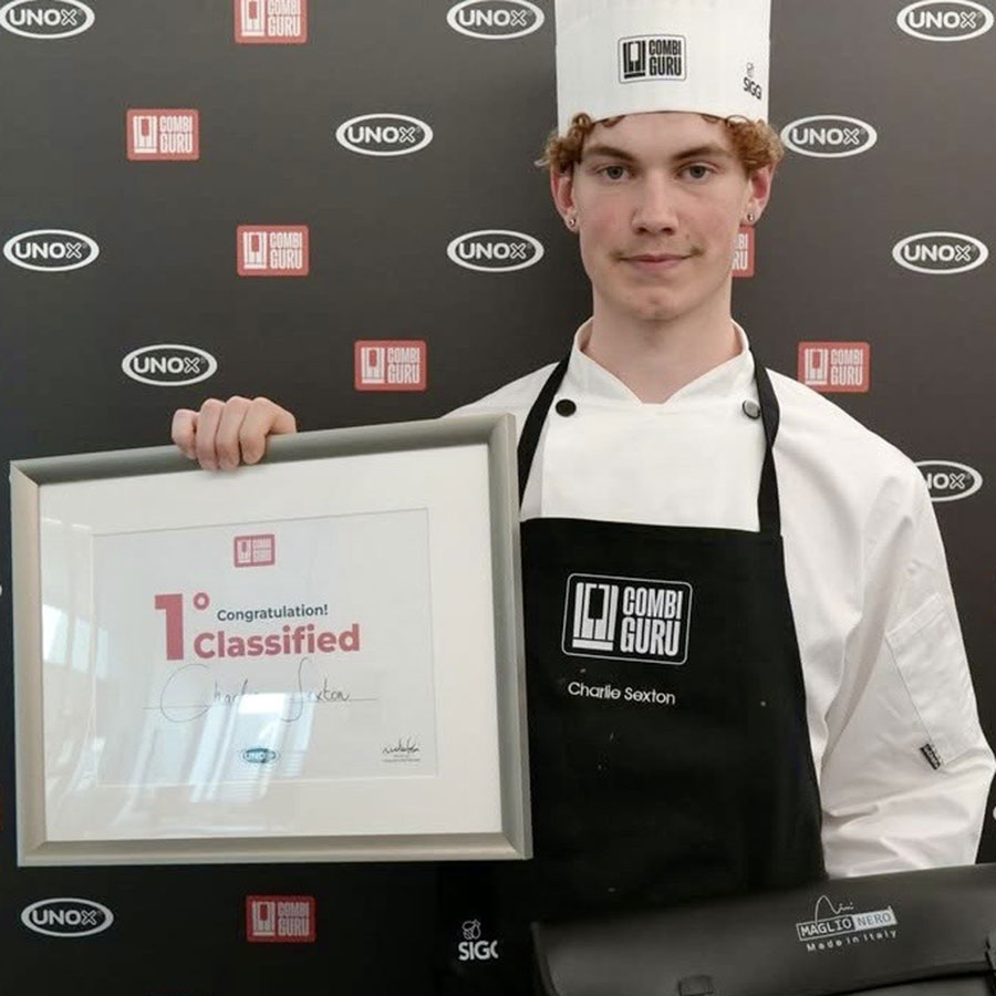 Student, Charlie Sexton, pictured wearing chef whites and hat, holding a framed certificate for winning the Combiguru Challenge
