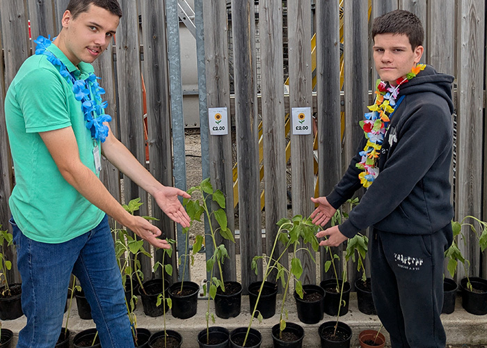 2 male foundation learning students with flower garlands round their necks, standing opposite each other, showing the plants they have grown