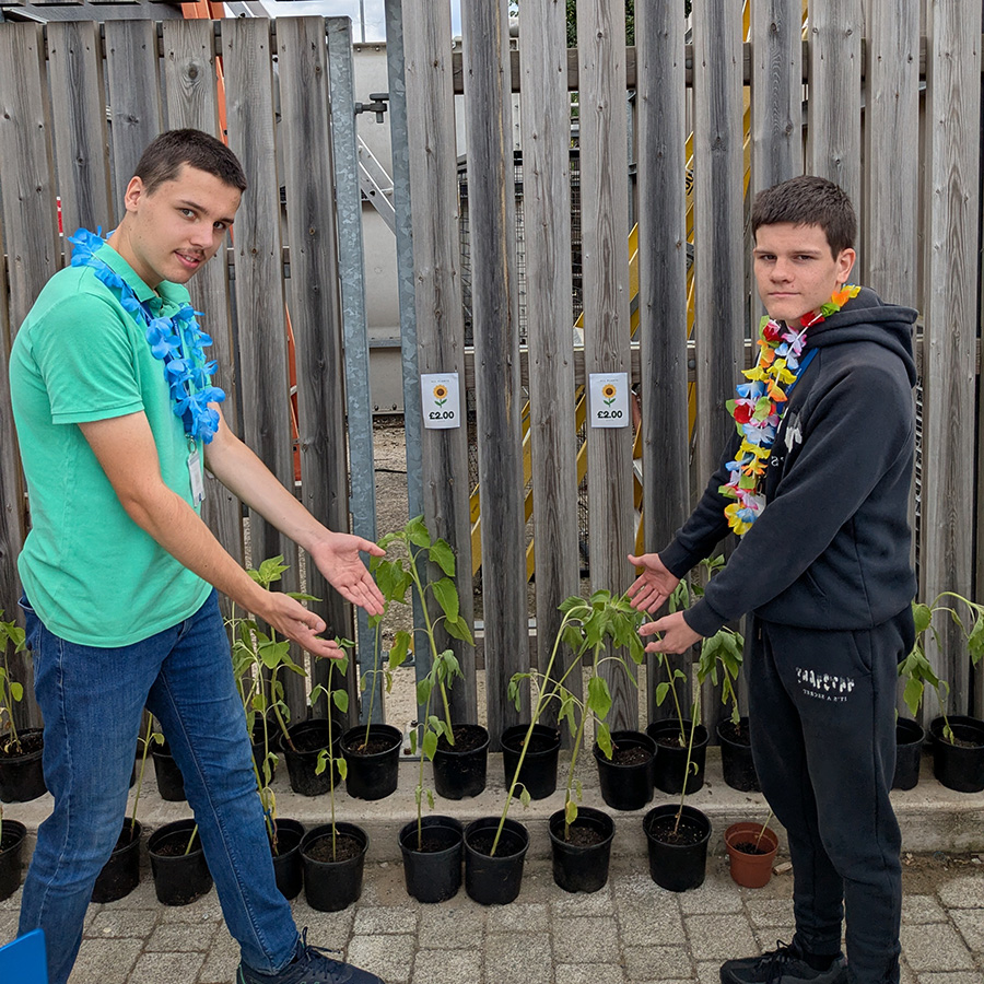 2 male foundation learning students with flower garlands round their necks, standing opposite each other, showing the plants they have grown